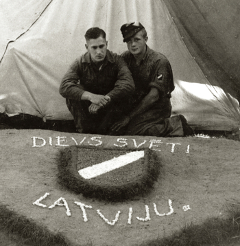 Internētie latviešu leģionāri pie pašdarināta rotājuma – latviešu leģiona vairodziņa. Ēkšes – Rennesletes nometne, 1945. gada
vasara.