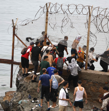 Pie žoga netālu no sadursmju vietas pie Fnidekas, uz Marokas un Spānijas robežas, 2026. gada 31. jūlijā pulcējušies cilvēki. Tūkstošiem migrantu nakts laikā no Marokas šķērsoja robežu un iekļuva Spānijas Ziemeļāfrikas anklāvā Seutā, 31. jūlijā pavēstīja policijas avots. 
