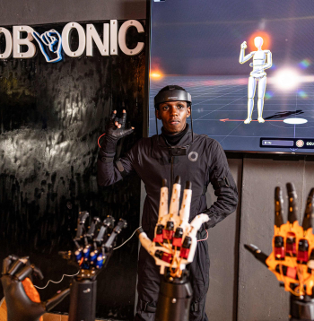 Robotikas inženieris Bens Kamau kustību uztveršanas tērpā demonstrē tā izmantošanu uzņēmuma “Zerobionic” darbnīcā Nairobi 2026. gada 19. augustā. Saskaņā ar Kenijas Nedzirdīgo bērnu biedrības datiem aptuveni 300 000 bērnu šajā Austrumāfrikas valstī ir dažādi dzirdes traucējumi, taču 2024. gadā tikai 20 000 no viņiem mācījās skolā. Šo problēmu cenšas risināt Kenijas jaunuzņēmums “Zerobionic”, kuru pirms trim gadiem līdzdibināja tolaik 22 gadus vecā Nora Kimati. Uzņēmuma futūristiskās robotrokas spēj zīmju valodā atveidot mutiski izteiktas norādes, kas ir īpaši svarīgi jauktajās klasēs, kurās nedzirdīgie skolēni bieži tiek atstāti novārtā. Robotrokas iespējams savienot ar īpašu tērpu, kas ieraksta nedzirdīgo skolotāju kustības, lai veidotu dabaszinātnēm, tehnoloģijām, inženierzinātnēm un matemātikai paredzētu zīmju datubāzi.