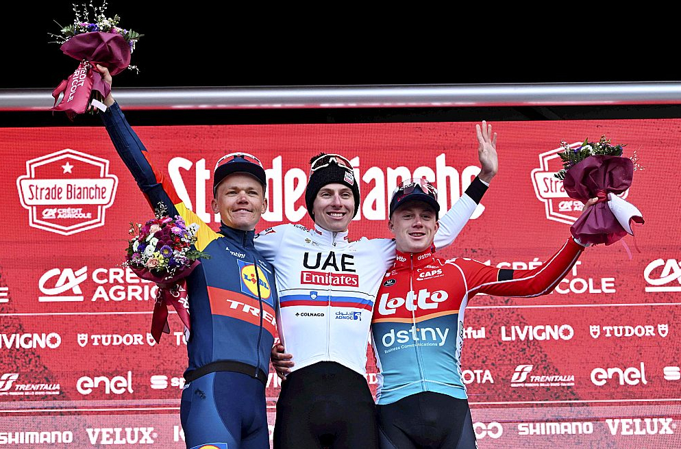 Latvietis Toms Skujiņš (no kreisās), slovēnis Tadejs Pogačars un beļģis Maksims van Fils uz fiziski grūto vienas dienas sacensību "Strade Bianche" goda pjedestāla.