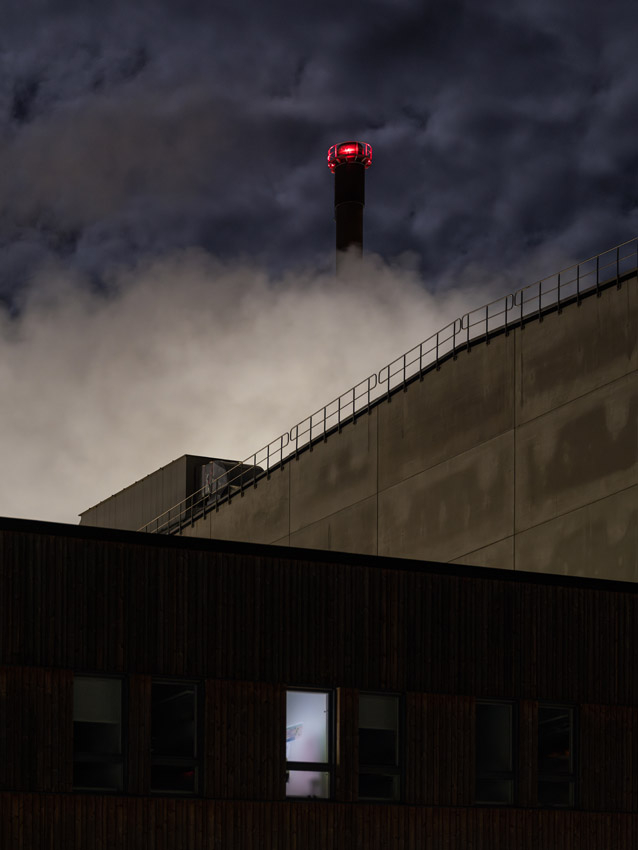 Papīrfabrika Obbolā, Zviedrijā, apņemta ar ēnu, betona un mākoņu slāņiem tumšā novembra naktī. 