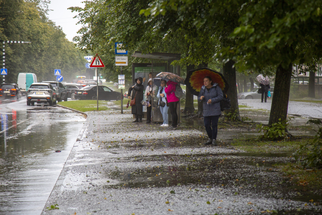 Cilvēki autobusa pieturā negaisa laikā Rīgā.