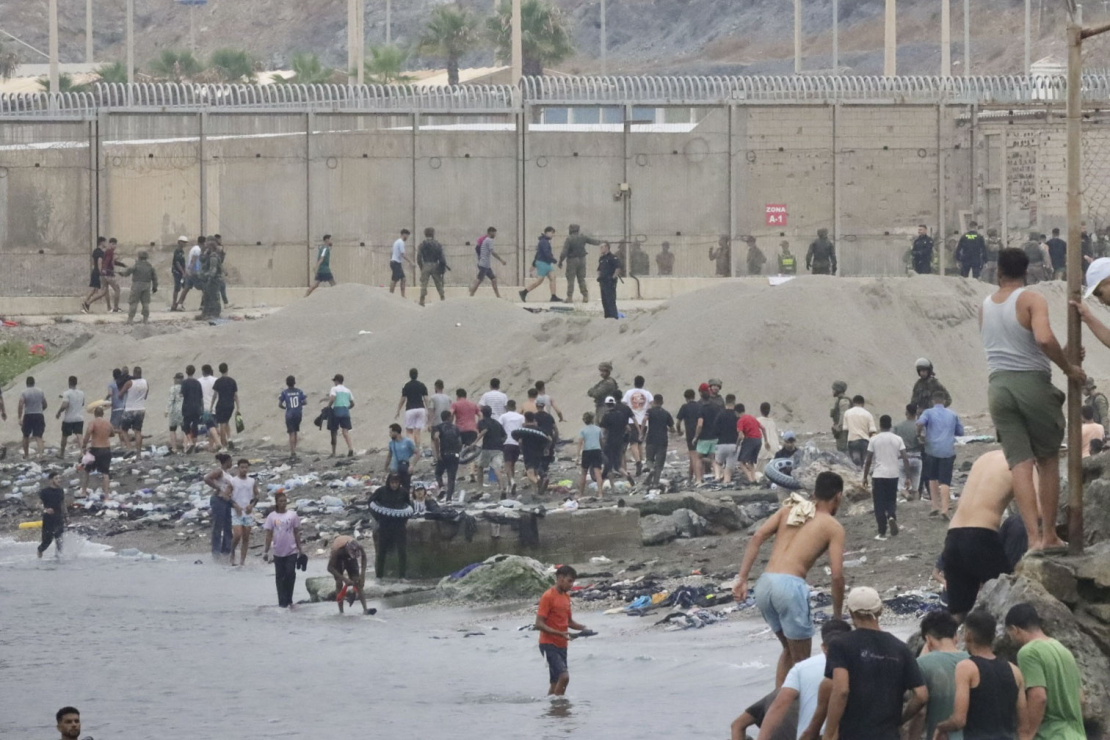 Pie žoga netālu no sadursmju vietas pie Fnidekas, uz Marokas un Spānijas robežas, 2026. gada 31. jūlijā pulcējušies cilvēki. Tūkstošiem migrantu nakts laikā no Marokas šķērsoja robežu un iekļuva Spānijas Ziemeļāfrikas anklāvā Seutā, 31. jūlijā pavēstīja policijas avots.