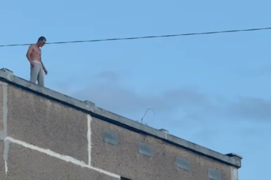 Aizturētais vīrietis uz daudzstāvu mājas jumta.