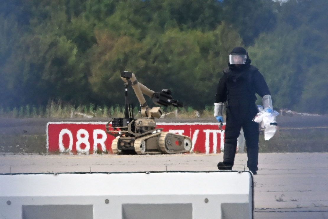 Kriminālistikas eksperts strādā līdzās policijas sapieru robotam pie Ukrainas kravas lidmašīnas Leipcigas/Halles lidostā Škeidicā, Vācijas austrumos, 2026. gada 5. augustā. Naktī lidmašīnas tuvumā tika atrasts ar sprāgstvielām aprīkots drons, bet netālu cita lidmašīna gaisā sadūrās ar nezināmu lidojošu objektu un pēc tam droši nolaidās.