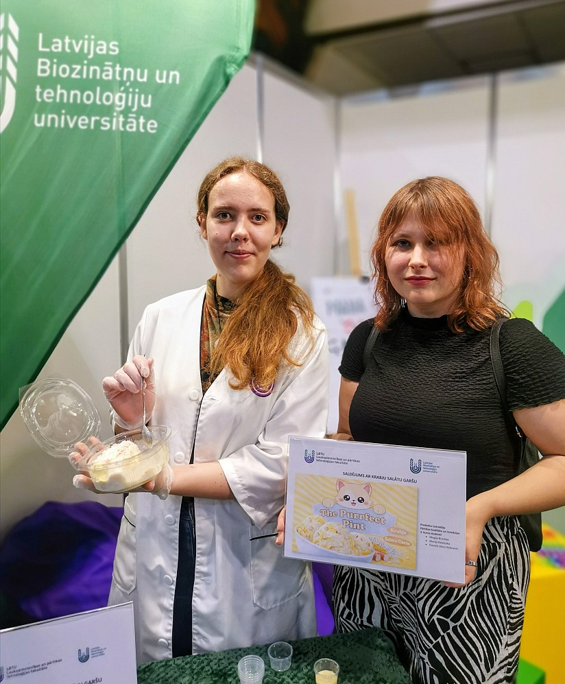 "Mums garšo krabju nūjiņu salāti, kāpēc lai neradītu saldējumu ar šādu garšu? Tas bija mūsu kursa darbs, par kuru saņēmām visaugstāko atzīmi," ir gandarītas Latvijas Biotehnoloģiju unversitātes Pārtikas kvalitātes un inovāciju studiju programmas trešā kursa studentes Marija Kalašņika un Megija Brasliņa, kuras piedāvā izstādes viesiem šo produktu nogaršot.