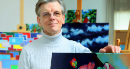 Einars Repše savā darbnīcā ar gleznu, kurai uzstādījumu sintezējis mākslīgais intelekts. Lūgums bijis izveidot kluso dabu ar ziediem un grāmatām spilgtās krāsās modernā izpildījumā.