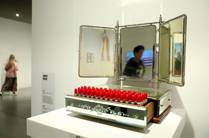 Sarmīte Māliņa, "Valoda". 1996. Topošā Latvijas Laikmetīgās mākslas muzeja kolekcija. Mēģinājums pētīt un saprast "sieviešu valodu", kas tiek izteikta caur spilgtām ārējām izpausmēm un krāsām. Māksliniece vērš kritiku ne tikai pret konstruēto sievišķību, kas nosaka, kā sievietei jāizskatās, jāuzvedas un jājūtas, bet arī sieviešu dalību šo normu realizācijā. Valoda ir daļa no triptiha, simboliski attēlojot pusmūžu sievietes dzīvē ar lūpu krāsām un spoguli.