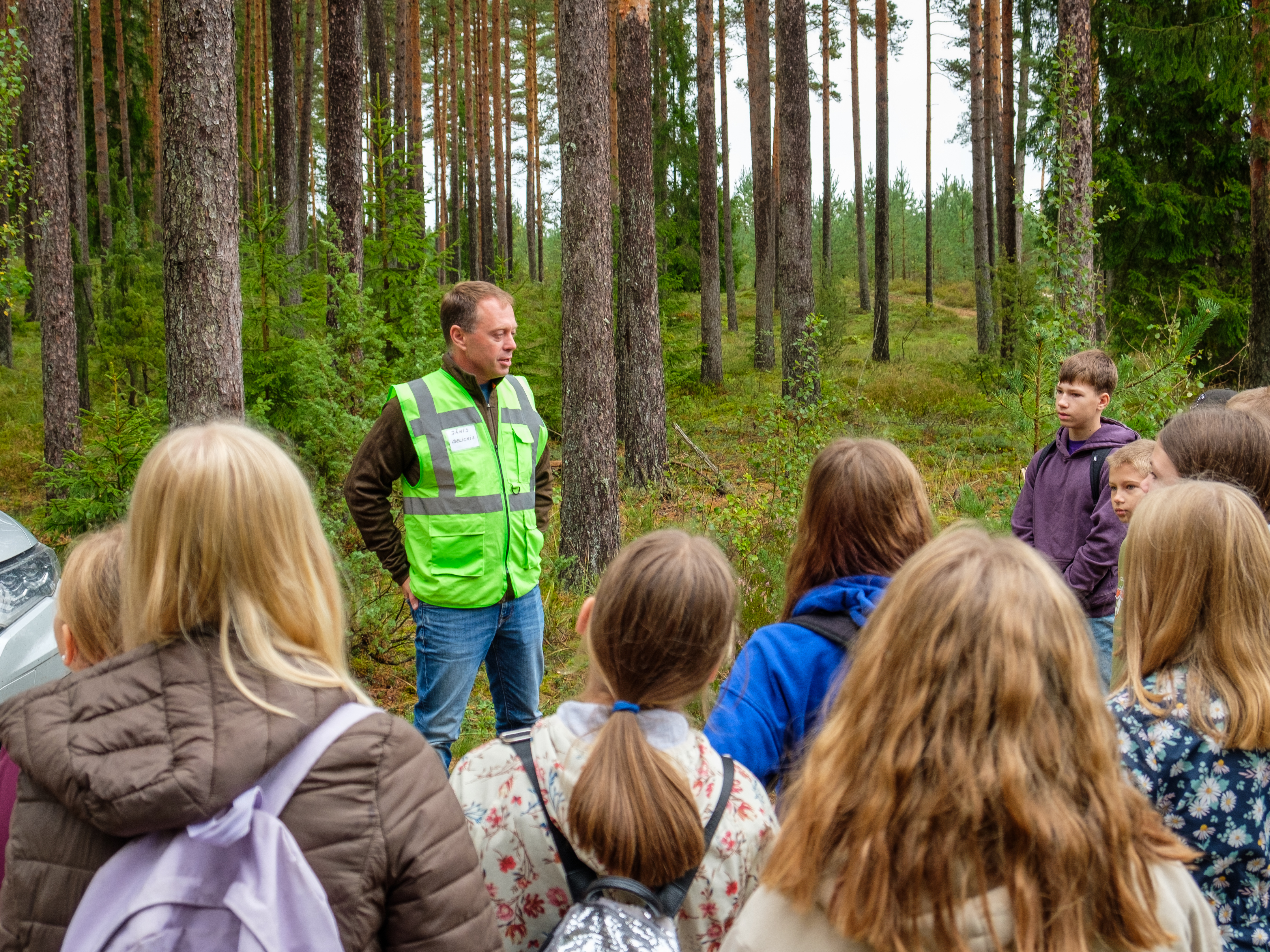 Daugmales skolēni ar interesi klausās LVM darbinieku stāstos par norisēm mežā.